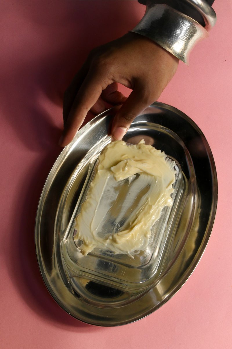 Hand hält eine Glasschale mit weicher heller Pflanzenbutter auf rosa Hintergrund