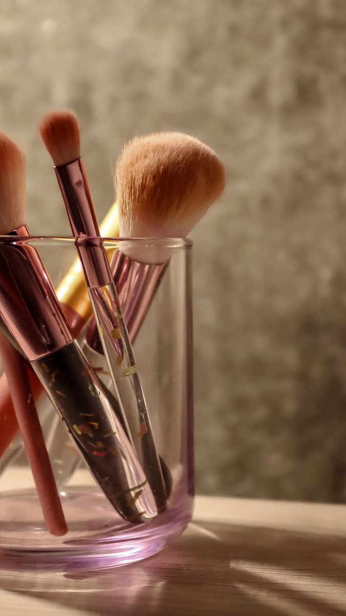 Make-up-Pinsel mit weichen Borsten und rosa Zwingen stehen in einem durchsichtigen Glas