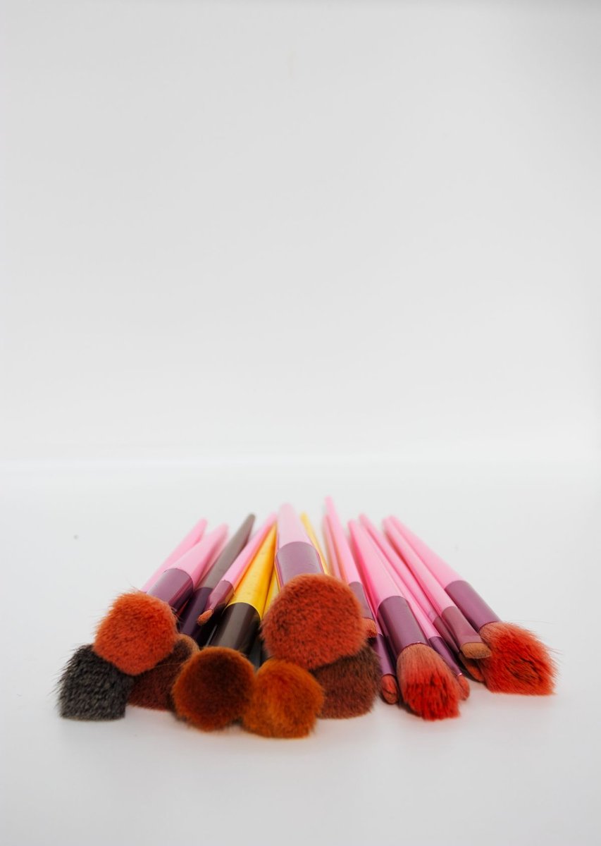 Gebündelte Make-up-Pinsel mit rosa Stielen und bunten Borsten vor weißem Hintergrund