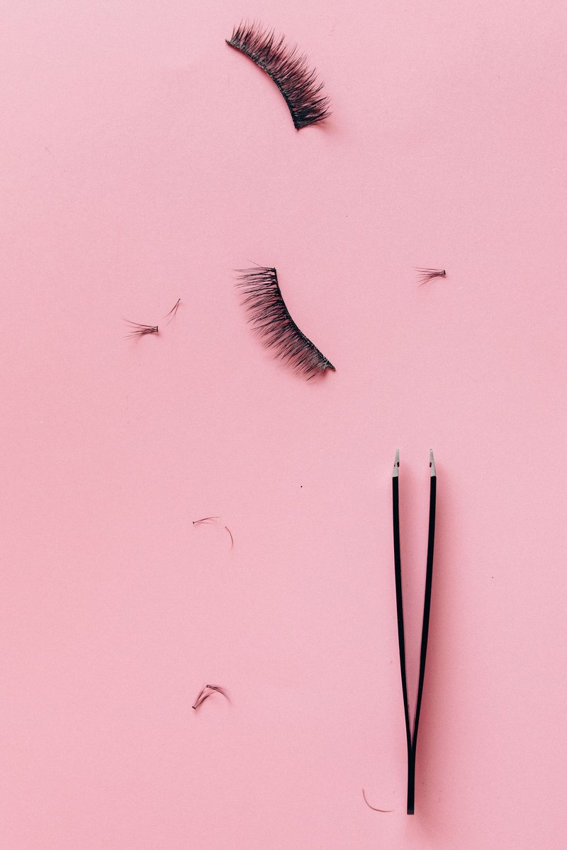Schwarze Pinzette neben künstlichen Wimpern und kleinen Wimpernbüscheln auf rosa Hintergrund