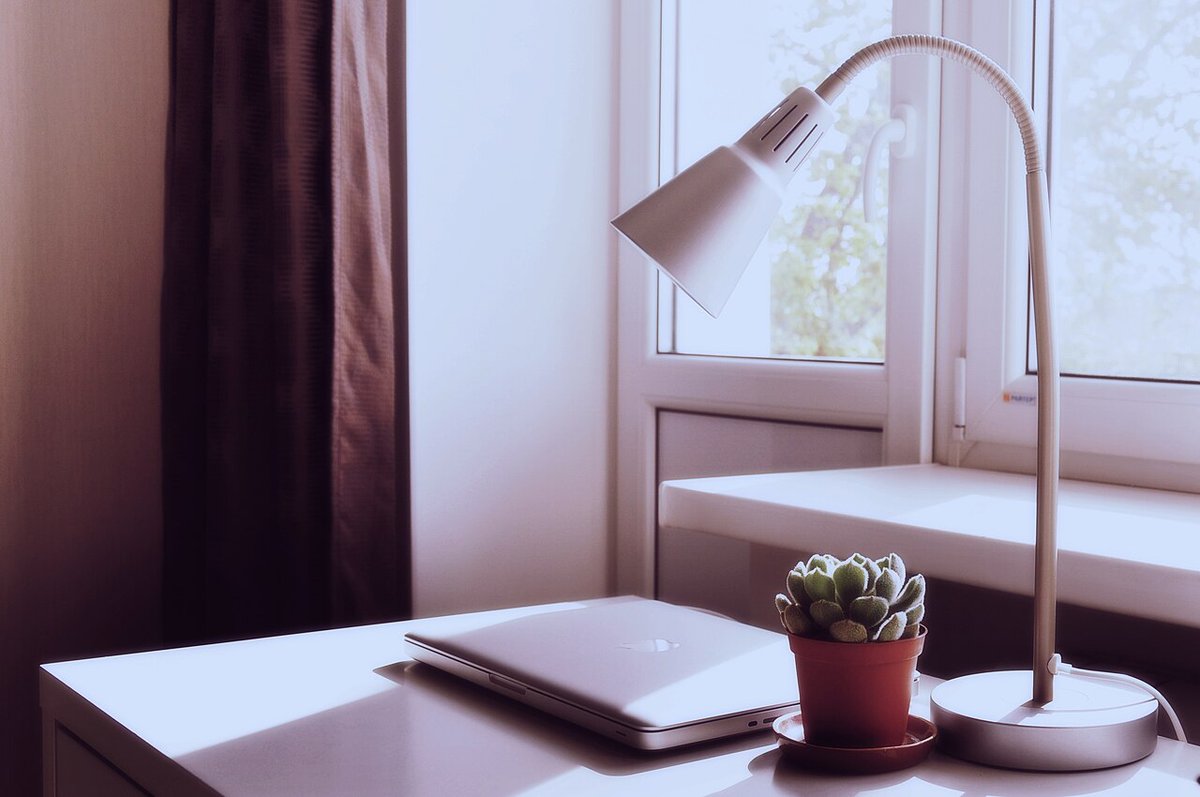 Schreibtisch mit Lampe, Laptop und kleiner Pflanze am Fenster