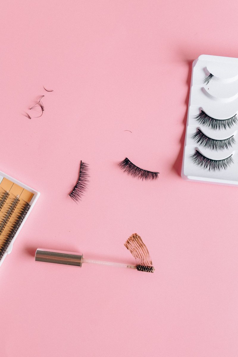 Mascara-Bürstchen mit Farbstrich, künstliche Wimpern und kleine Wimpernbüschel auf rosa Hintergrund